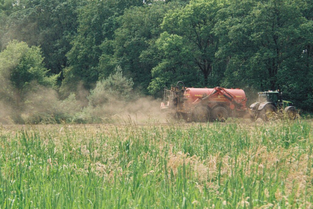 Tractor rijdt dierlijke mest uit op een akker, een praktijk die kan bijdragen aan stikstofoverschotten en andere milieuproblemen.